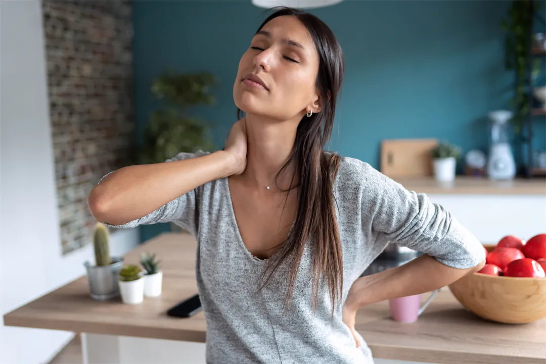 LIFEORIA A woman experiencing neck pain while cooking in the kitchen.